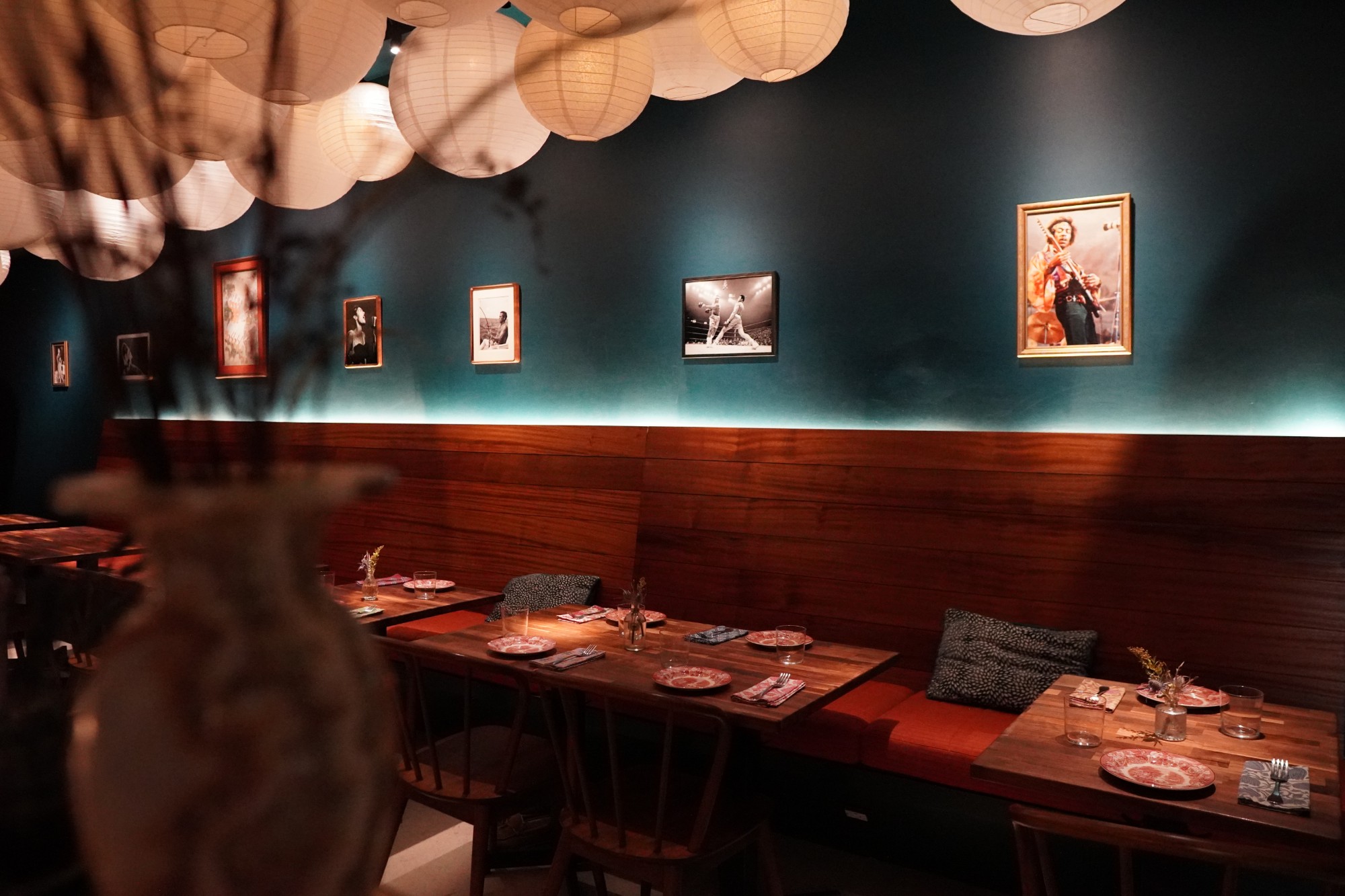 Paper lanterns over the banquette and framed photos on a teal wall